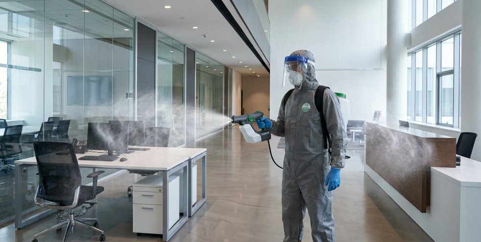 Worker spraying electrostatic disinfectant in a modern office building